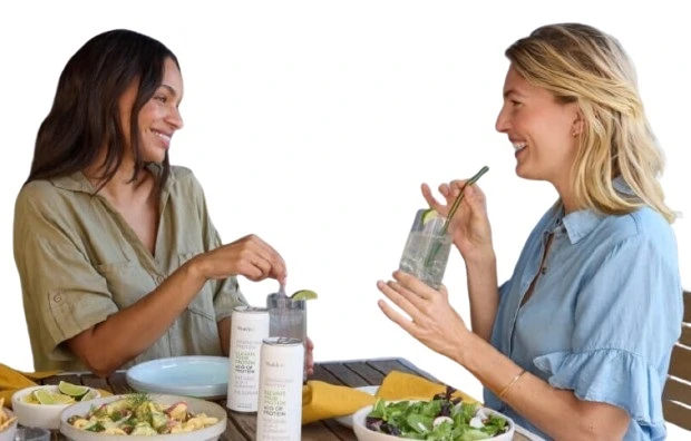 Join-Shaklee-New-Zealand-Shaklee_Ambassador - Shaklee NZ - Shaklee NZ Two women smiling and talking at a table with salads and drinks on a sunny day.